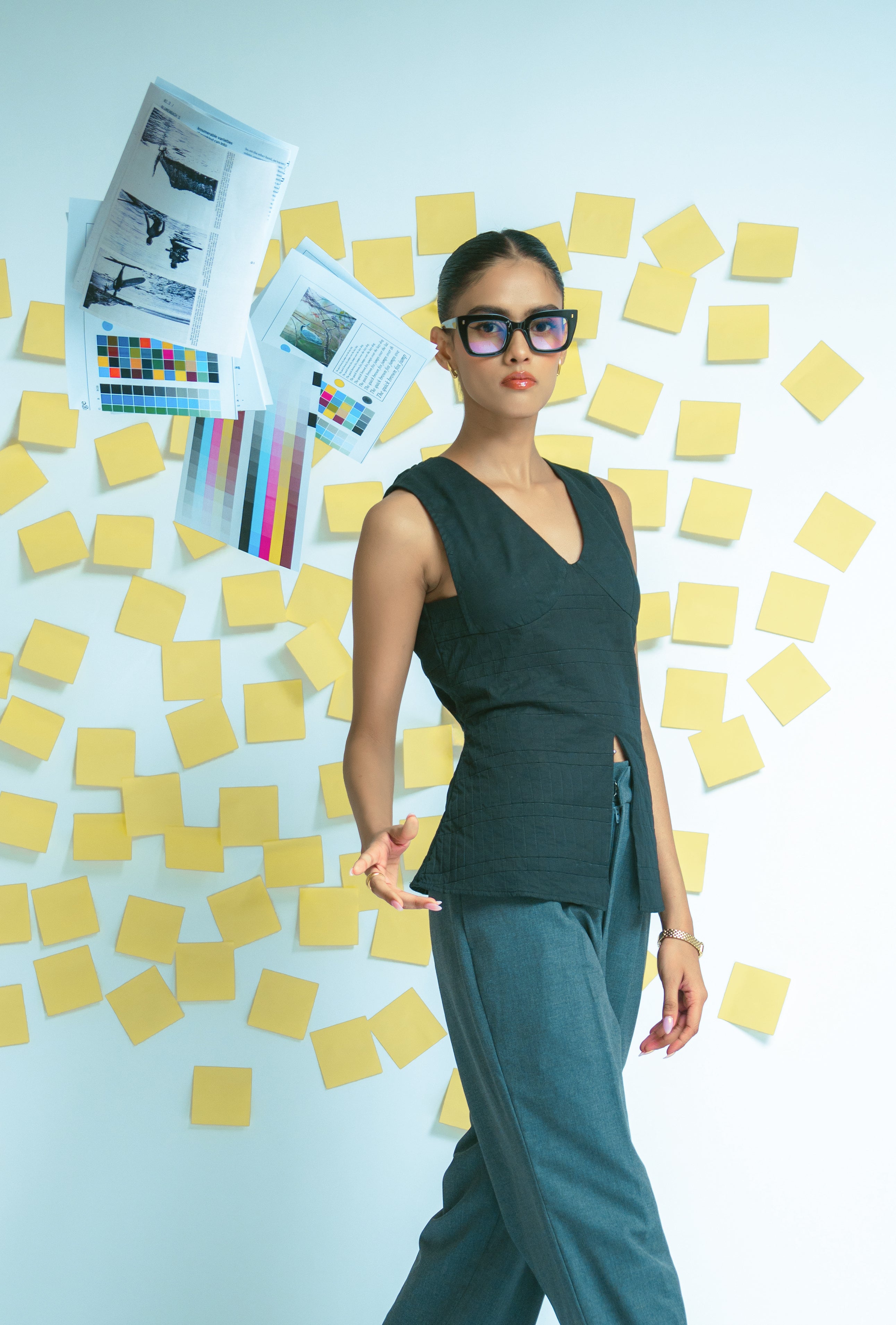 Woman in a Black Top and Grey pant outfit standing in front of yellow sticky notes and design materials.