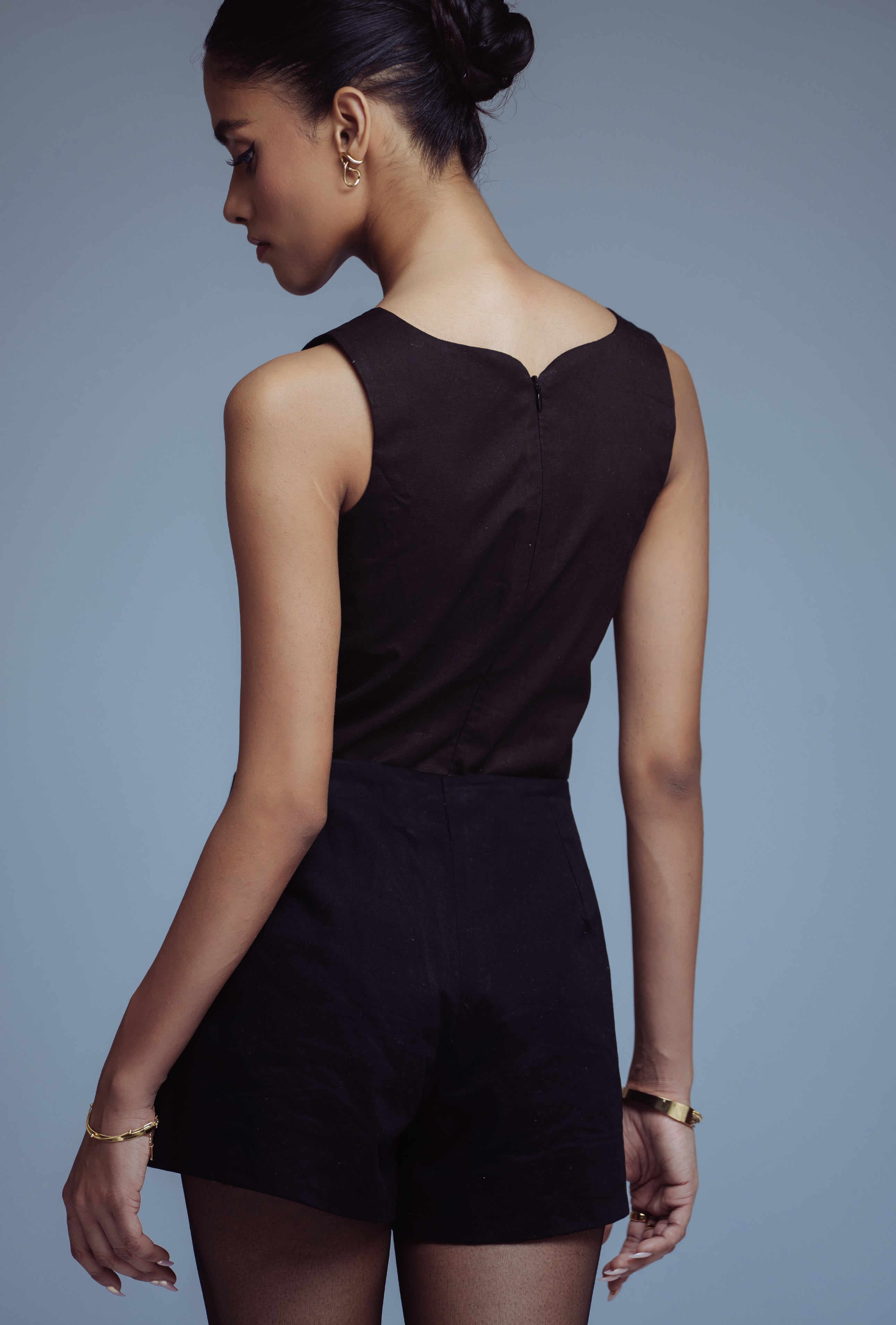 Woman wearing a black sleeveless top and shorts against a gray background