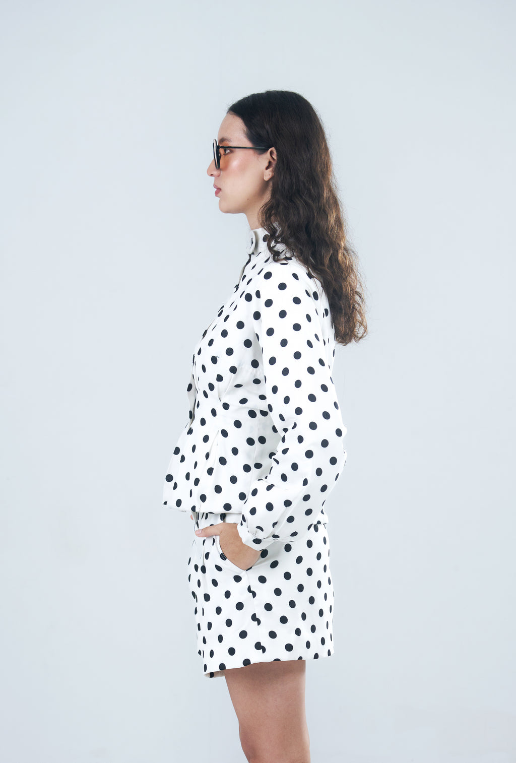 Woman wearing a white jacket with black polka dots against a light gray background